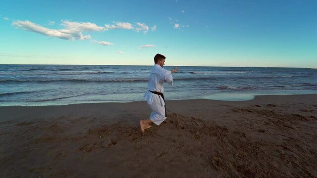 Karate fighter practicing a kata on the beach at sunset. Karate fighter practicing technique kicking and punching hard and fast. 4K video