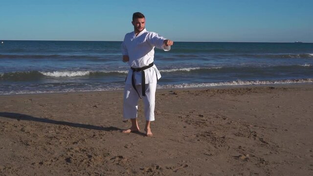Karate fighter practicing kata on the beach at sunset and doing jumping, balancing and defense techniques in the open air. Wado ryu style. Truck right camera movement recorded in slow motion. kata