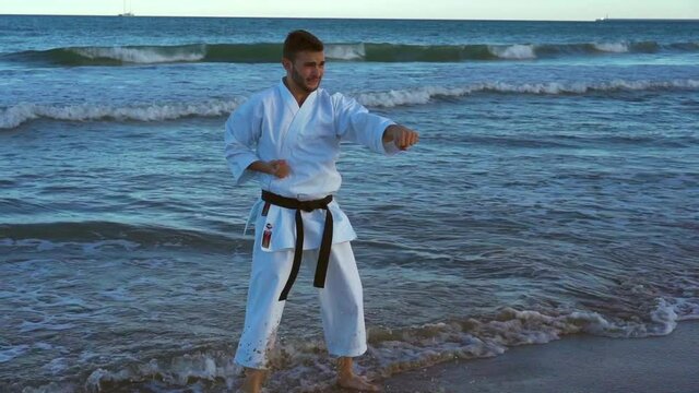 Karate fighter practicing technique on the seashore with his feet in the water at sunset. Karate wado ryu. traditional karate. slow motion