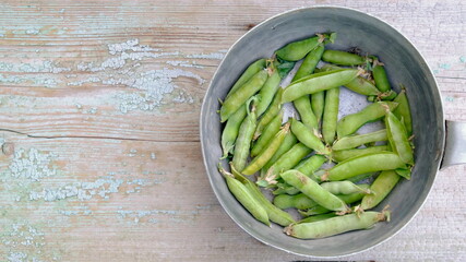 Pea pods in aliminium dish on wooden background