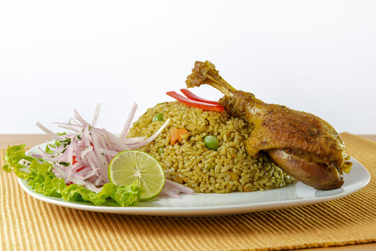 Peruvian food, rice with duck, accompanied by onion, lemon and lettuce. White background.