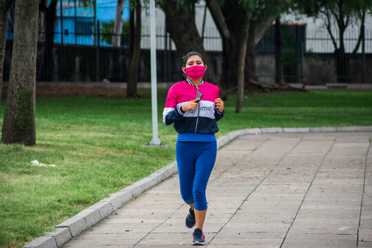 mujer joven con cubrebocas corriendo en el parque mirando hacia la c&aacute;mara