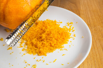 A zester zesting orange skin on a white plate on a wooden tabletop. 