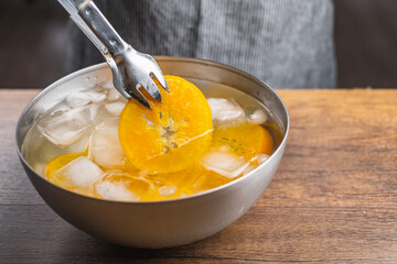 Putting cooked orange slices with a tongs in ice water to cool down after cooking in hot water.