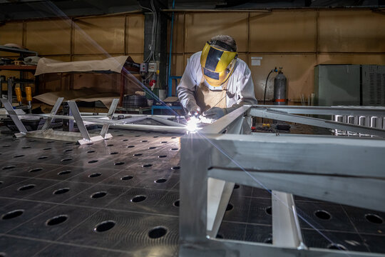 worker welds aluminum parts. Metalworking plant, the wizard in the mask