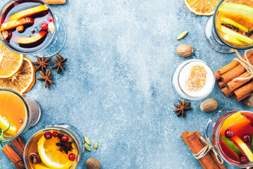Various autumn or winter seasonal alcohol hot cocktails - mulled wine, glogg, grog, eggnog, warm ginger ale, hot buttered rum, punch, mulled apple cider on gray background, top view with copy space