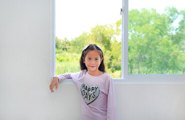 Portrait of little asian kid girl lies at window of house.