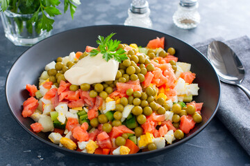 Salad with red fish, Olivier, in a black bowl on the table, selective focus