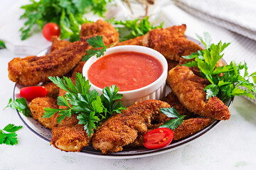 Breaded mini chicken fillets served with tomato sauce. American food. Chicken nuggets with parsley.