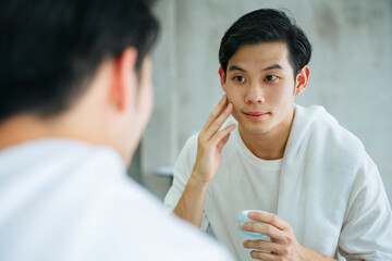 Young man apply facial cream lotion at mirror in bathroom.
