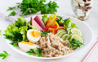 Breakfast oatmeal porridge with boiled egg, ham and vegetables salad. Healthy food.