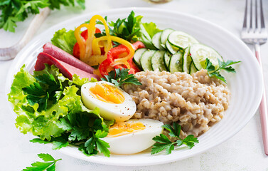 Breakfast oatmeal porridge with boiled egg, ham and vegetables salad. Healthy food.