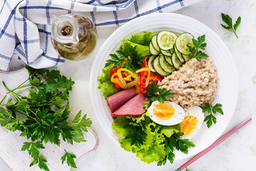 Breakfast oatmeal porridge with boiled egg, ham and vegetables salad. Healthy food. Top view, overhead,  copy space
