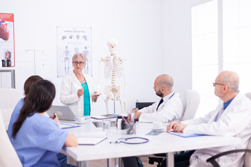 Medical scientist doing demonstration with human skeleton in conference room with her team. Clinic...