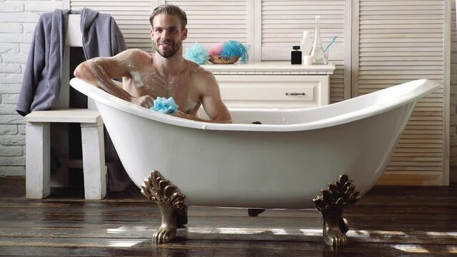 Happy young man washing in bathrobe in bathroom. Hygiene and spa. Care of skin, morning. Naked guy with bare torso.