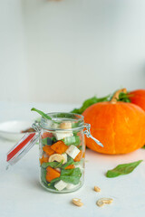 Bright autumn salad of pumpkin, spinach and feta in a jar. A good snack on the road. Salad and ingredients on a light background. 