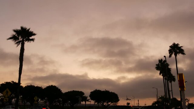 Airplane landing in LAX airport at sunset, Los Angeles, California USA. Passenger flight or cargo plane silhouette, dramatic cloudscape. Aircraft arrival to airfield. International transport flying.