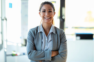 Smiling young businesswoman looking at camera while standing in the office.