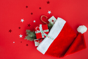Santa Claus hat with gifts and Christmas sweets on a bright red background decorated with shiny stars. Flatly.