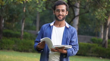 Happy indian male student holding smartphone sitting outdoor Indian Student with a backpack