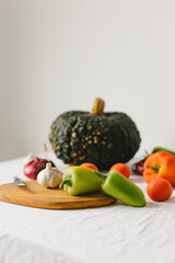 Still life on the table. Large green pumpkin, pepper, garlic, red onion, tomato, wooden board and knife in the kitchen. Stylish composition.