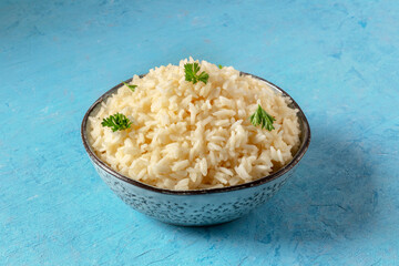 A bowl of boiled rice with fresh parsley leaves, on a blue background