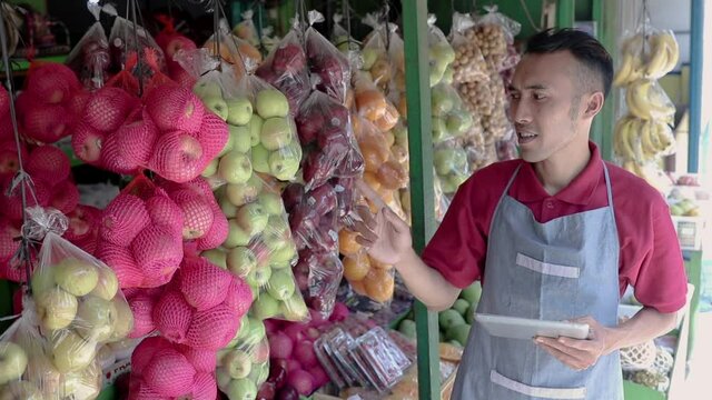 a male shop owner holding a digital tablet while observing fresh fruit in a fruit shop
