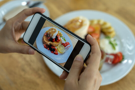 Woman's hand is taking a picture of a strawberry pancake with a smartphone. Women are taking photos to post or share popular dishes for social media.