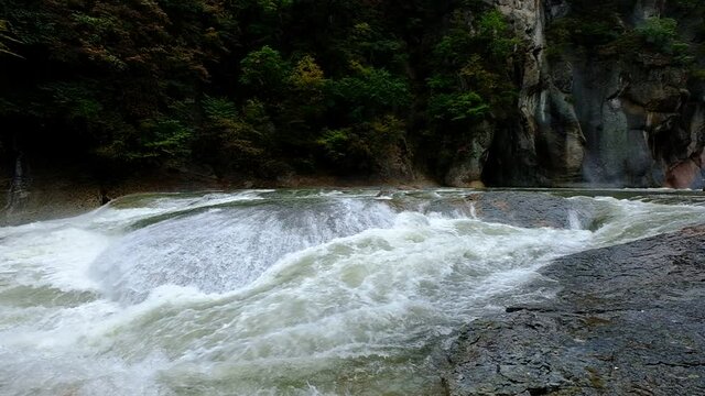 A panoramic slow motion of a large water stream that flows noisily in a huge rocky environment, Fukiware Falls, next to Numata, near Nikko National Park, Japan.