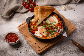 Shakshouka in cast iron skillet. Fried eggs with vegetables and toasts.