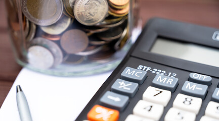 Jar with coins on notebook with pen,calculator on wooden background.