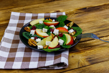 Autumn spinach salad with apple, feta cheese, walnut and dried cranberry on wooden table. Healthy vegetarian food