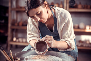 Beautiful female master making pottery, sculptor from wet clay on wheel. Handicraft industry.