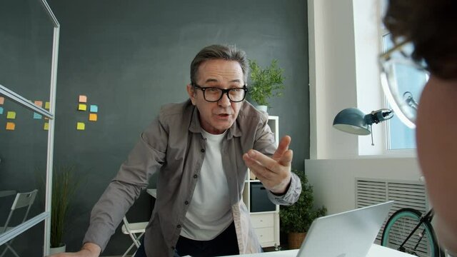 Angry businessman is yelling at female employee throwing papers during meeting in office. Corporate relationship and negative emotions concept.