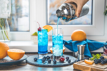 Real woman preparing a blue gin tonic cocktail with ice a mix of alcohol near the window on the...