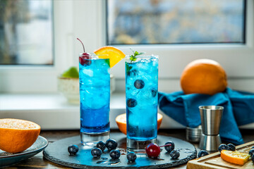Two glasses of blue gin tonic cocktail with ice a mix of alcohol near the window on the table near...