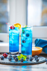 Two glasses of blue gin tonic cocktail with ice a mix of alcohol near the window on the table near...