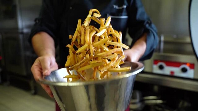 Chef seasoning french fries in a big bowl, in a restaurant kitchen