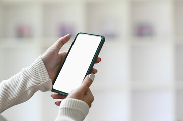 A mock up smartphone blank screen in female hands with blurred office interior background.