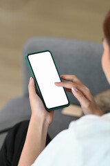 Cropped shot of young woman using smart phone with blank screen and sitting on a couch in the living room.