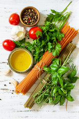 Ingredients for italy cuisine. Tomato and spinach spaghetti, herbs spices, olive oil and vegetables on a table. Top view flat lay background.