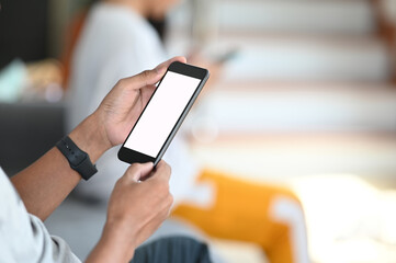 Cropped shot of male worker using mock up smartphone while relaxed on sofa in living room.