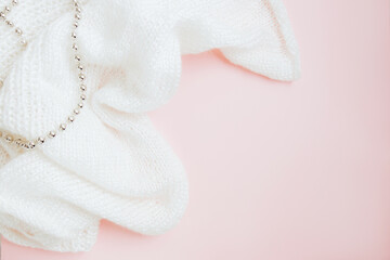 White knitted fabric and and silver beads on pink background. Craft on black background. Knitwear as a concept of female hobby. Copy space