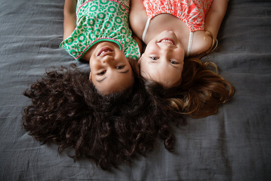 Portrait of smiling young girls lying upside down on bed - Powered by Adobe