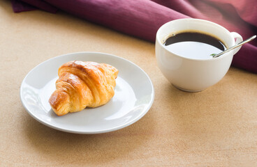 Croissant on white plate and coffee cup.