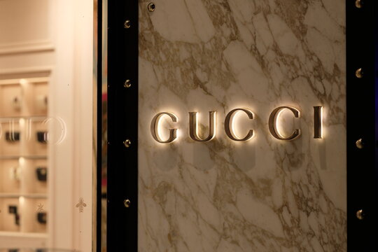 Shanghai/China-July 2019: close up shining GUCCI logo on granite wall outside store at night. Defocused products in store. A famous Italian luxury brand of fashion and leather goods.