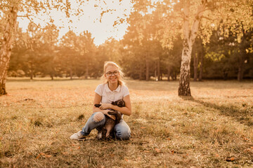 Naklejka na ściany i meble Teenager blonde girl with big glasses laughing and playing with little puppy spaniel in the warm park