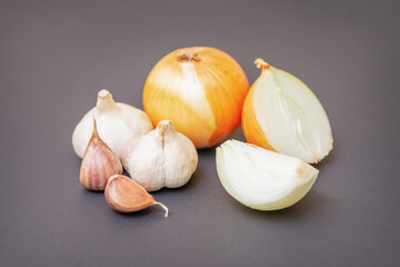 Unpeeled raw bulb and clove of garlic and onion on black surface with empty space for text