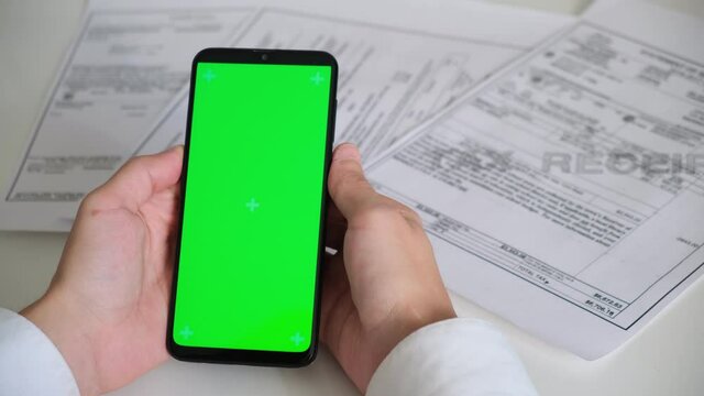 Phone with green screen and payment receipts, tax documents on white background top View . smartphone chromakey swipes in different directions. copy space. High quality 4k footage