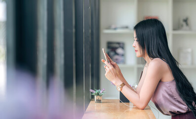 Young beautiful asian woman using smartphone while sitting at counter table in cafe, copy space.